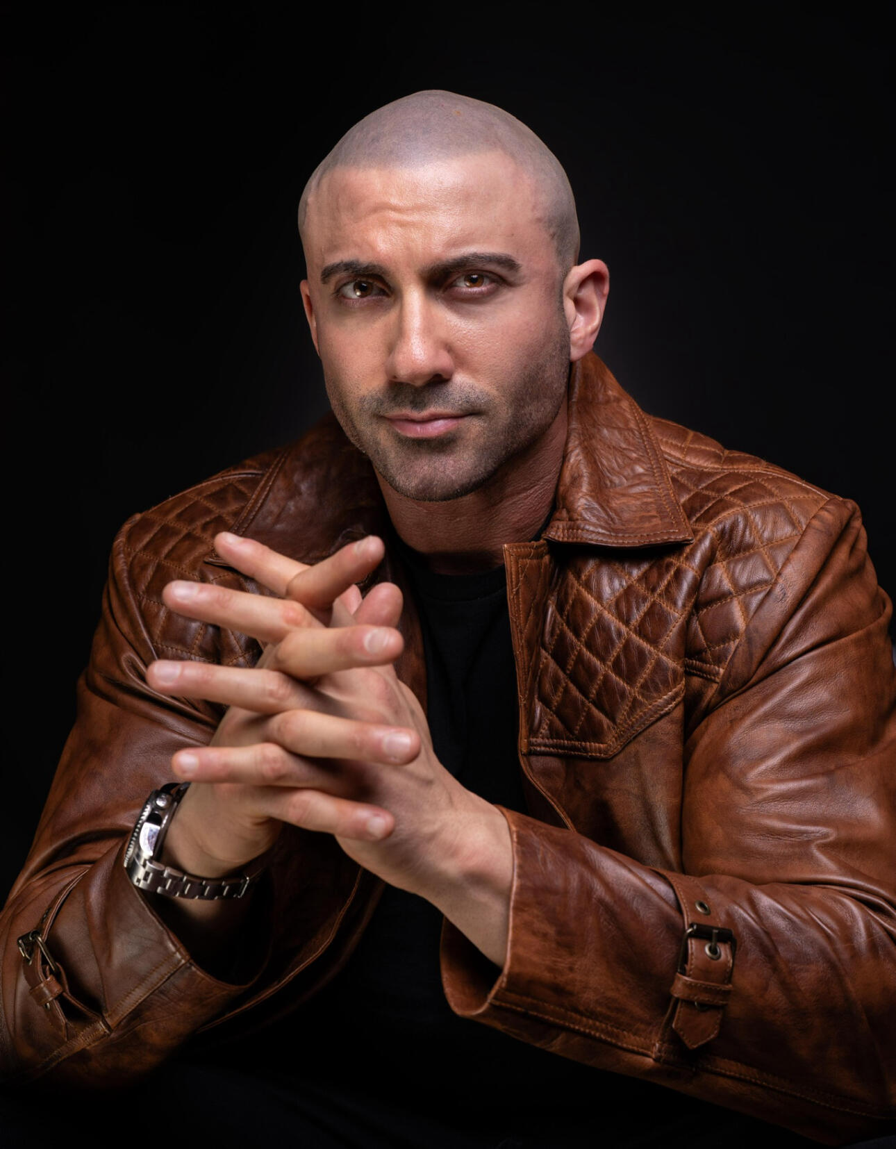 Tom Rooney Author, Founder, Headline Performer Author Thomas Rooney (Tom Rooney) sitting with clasped hands promoting his book Reflections of a Male Revue Headliner: How to Win at Life and Love, wearing a brown leather blazer